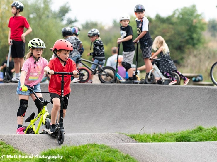 A group of kids play on a scooters park in Exeter during the Cranbrook Pump Track launch event in September 2024. Image credited to Matt Round Photography.